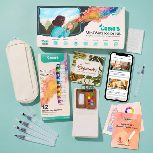 Tobio's Mini Watercolor Kit laid out with its illustrated box, walnut palette, 12-color paint pack, beginner's workbook, and water brushes.