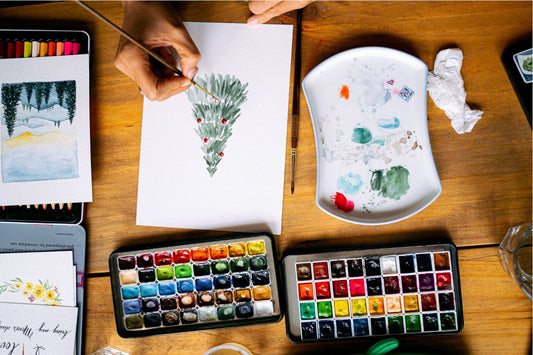 Person making a watercolor painting of a Christmas tree