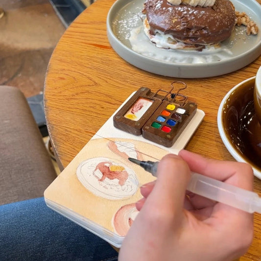 Painting in a mini sketchbook with a compact Tobio's watercolor kit at a cafe