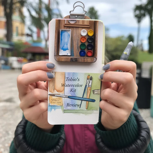 Person holding Tobio's Watercolor Kit with mini paint pots, water brush, and illustrated review card