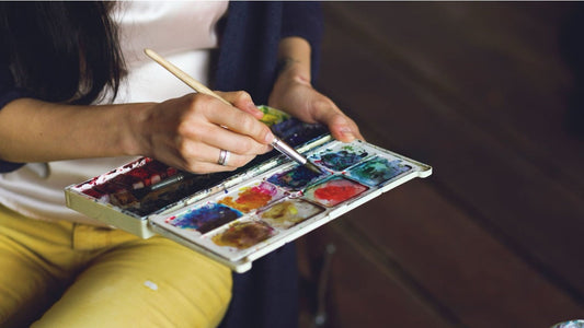 Woman holding her watercolor palette while mixing paint on it 