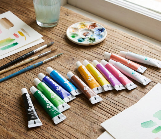 Tobio's 12 watercolor paint tubes on a table with brushes and swatches