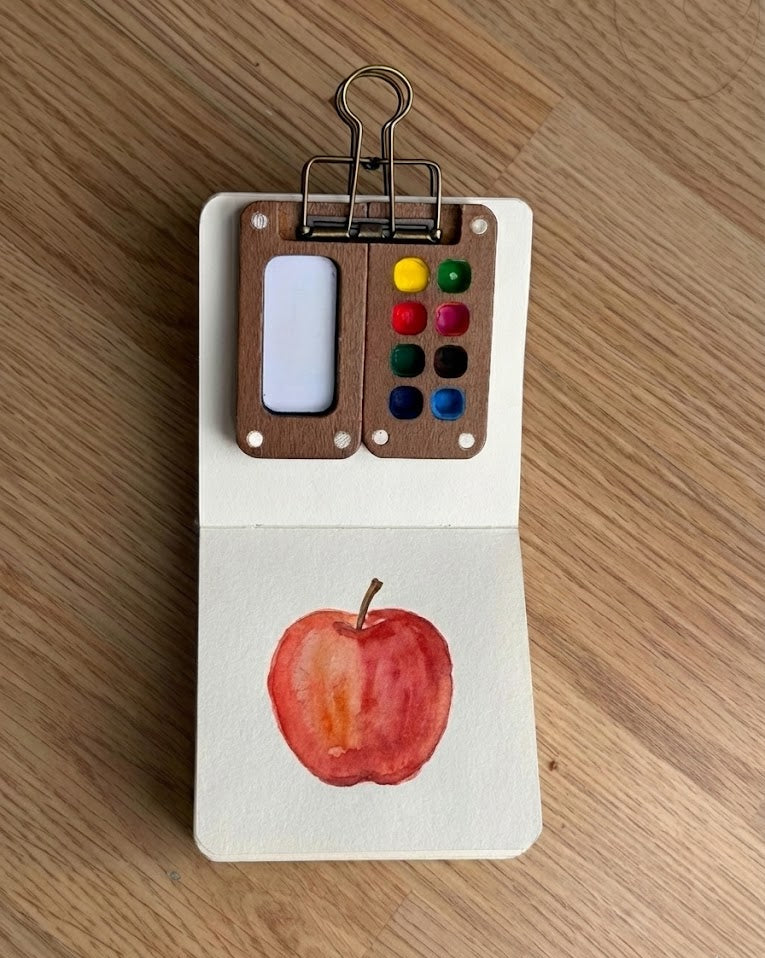 Tobio’s Kits apple watercolor painting, showing red washes and simple details in a sketchbook.