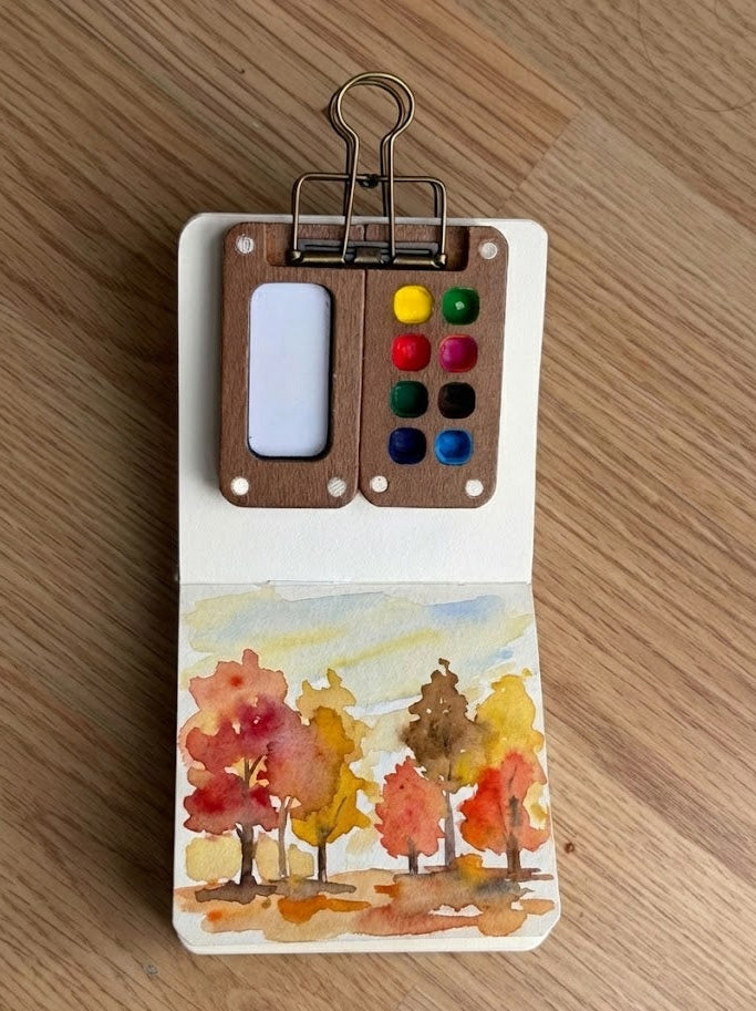 Small paint palette with watercolor trees on a wooden surface