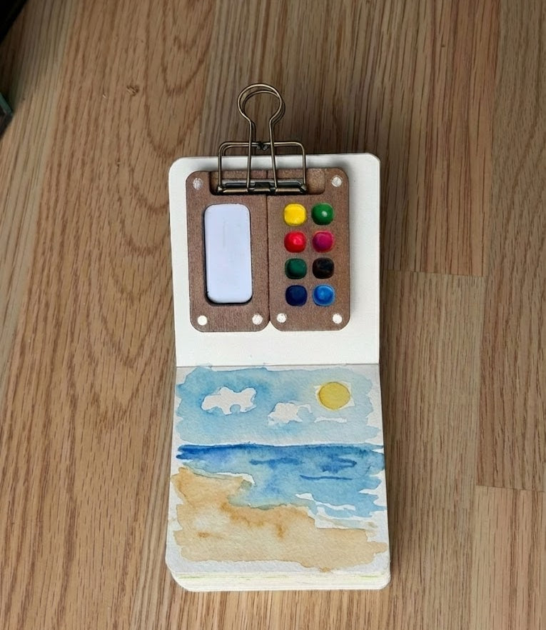 A watercolor painting of a beach with a colorful palette on a wooden surface
