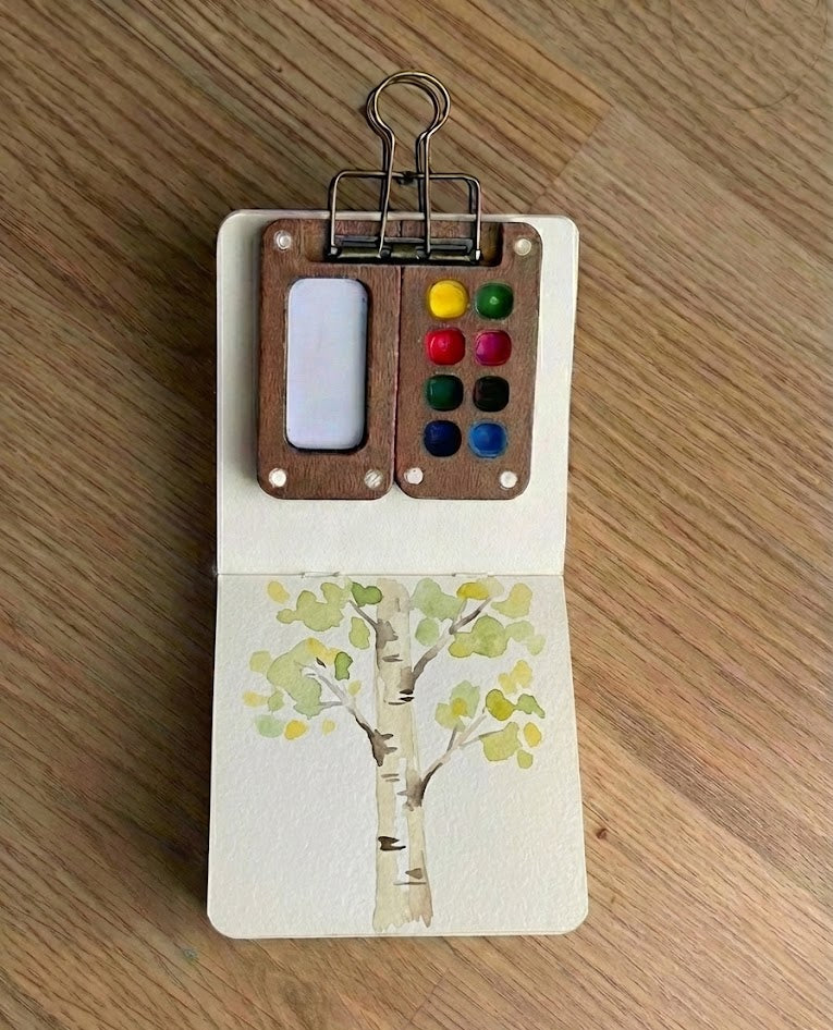 Small wooden art set with paint palette and birch tree watercolor painting on a wooden surface