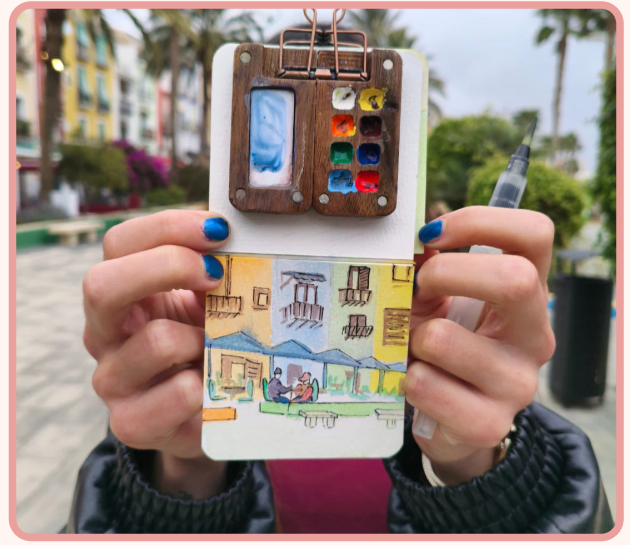 Hands holding Tobio's watercolor kit with colorful city painting