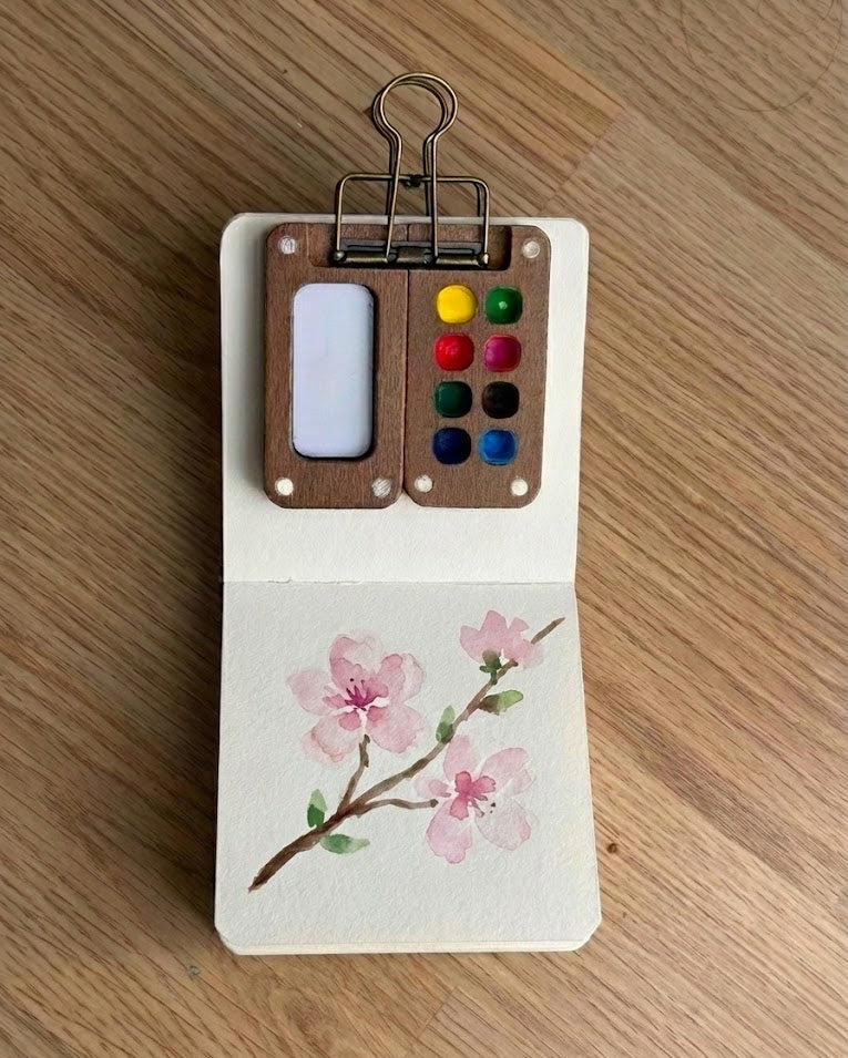 Small paint set with watercolor paper featuring a floral design on a wooden surface