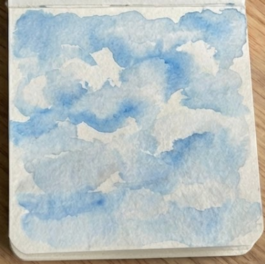 A sketchbook study of watercolor clouds where pigment has been lifted to soften the edges of the white cloud forms.