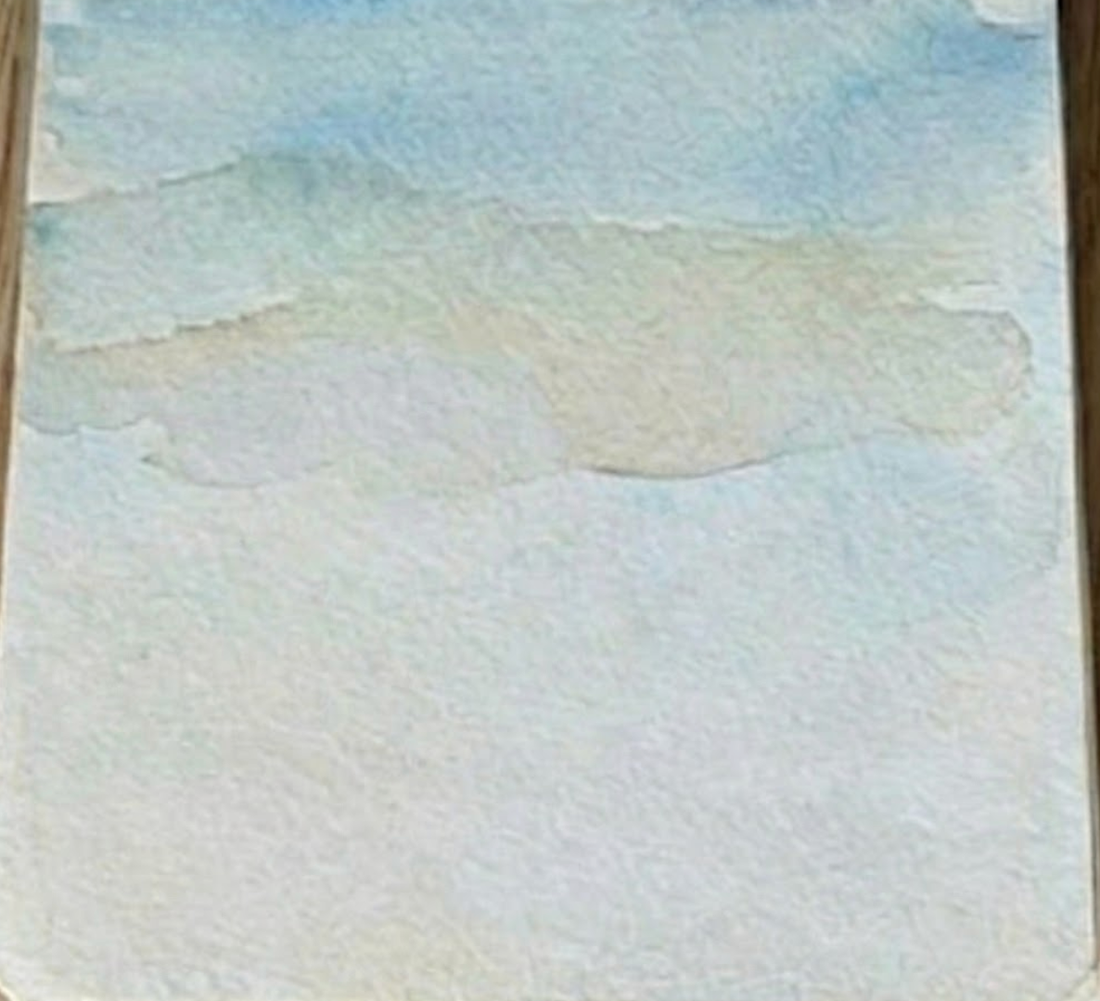 Adding hazy blue mountains in step two of a desert watercolor painting.
