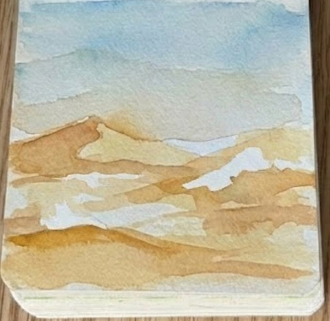 Painting warm yellow sand dunes for step three of a desert watercolor painting.
