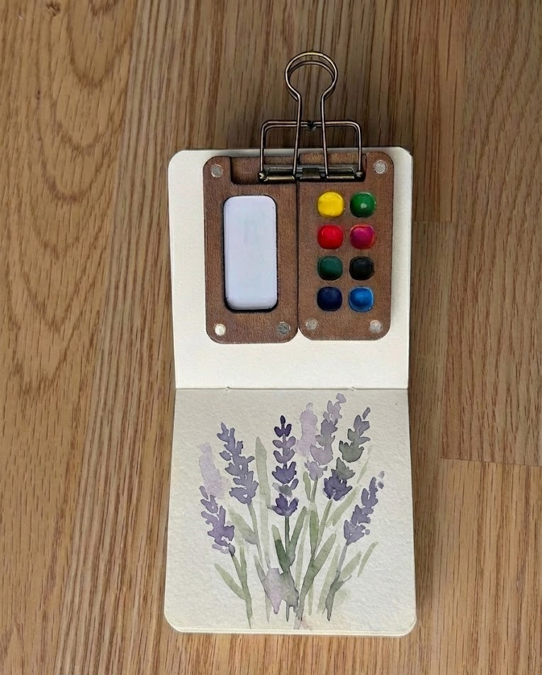 Soft lavender watercolor painting with muted green stems in a sketchbook, painted with Tobio’s Kits.