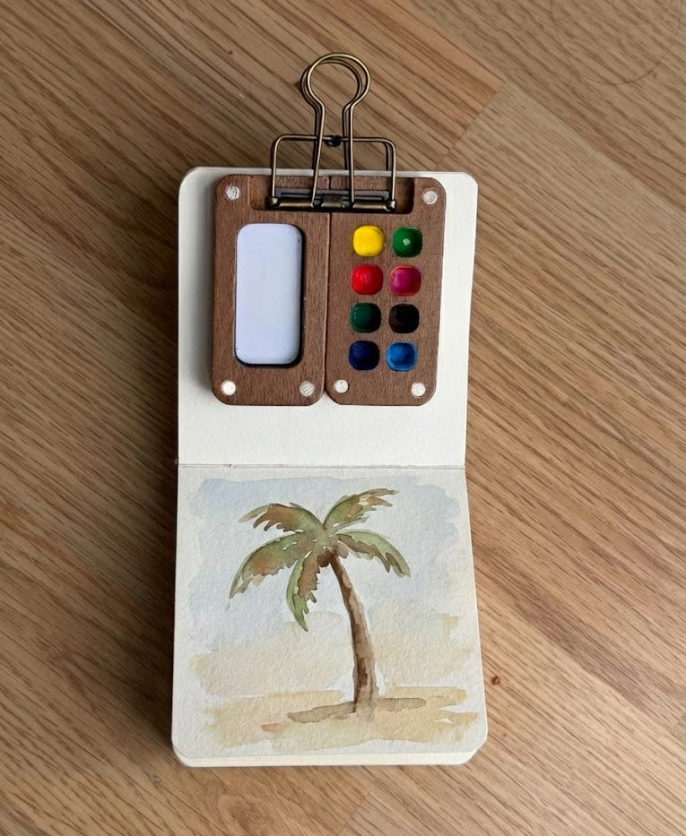 Small paint kit with a palm tree painting on a wooden surface