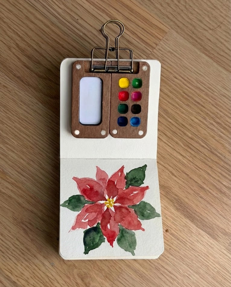 Small paint palette with watercolor flowers on a wooden surface