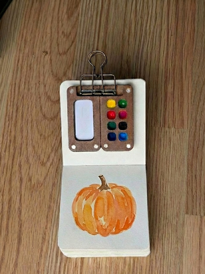 Tobio's Kits pumpkin watercolor painting, painted in a small watercolor sketchbook with soft washes and simple details.