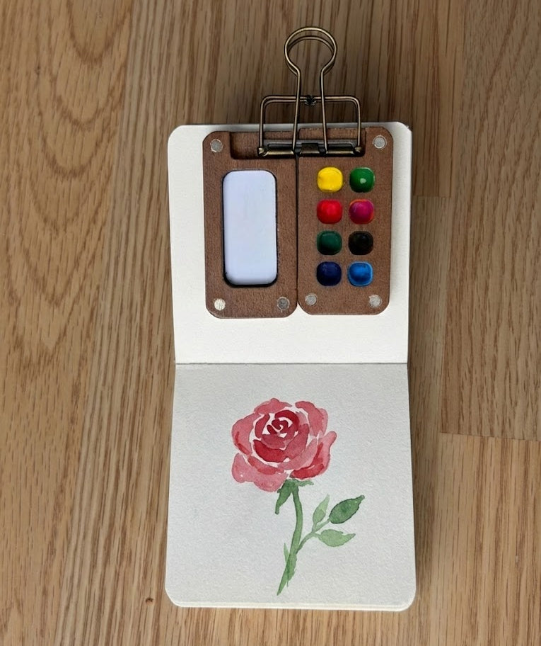 Small art book with watercolor paint palette and red rose watercolor painting 