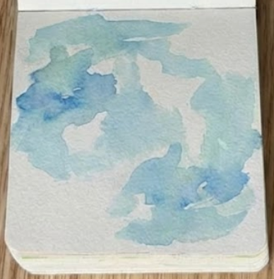 Sketchbook page showing an initial loose, splashy blue watercolor background wash.