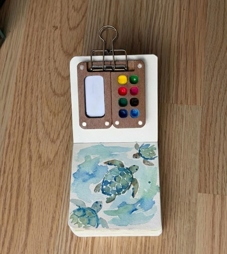 Small open book with a watercolor painting of sea turtles 