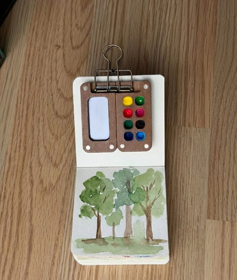 Small notebook with watercolor trees on a wooden surface