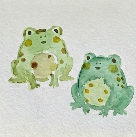 Completed detailed watercolor paintings of frogs sketchbook study with defined circular eyes, pupils, simple curved smiles, and a specific cluster of spots.