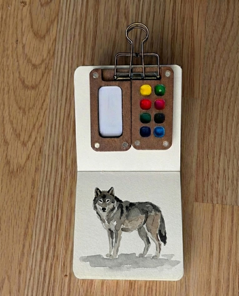 Watercolor wolf painting in a mini sketchbook with a portable wooden palette.